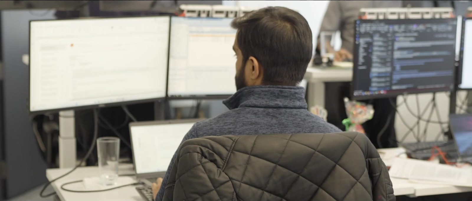 A man at a desk with several monitors, one showing code