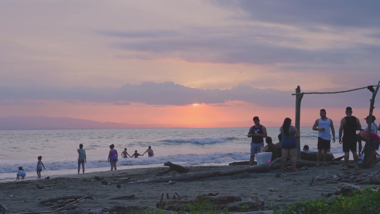 People on a beach at sunset beside a driftwood frame