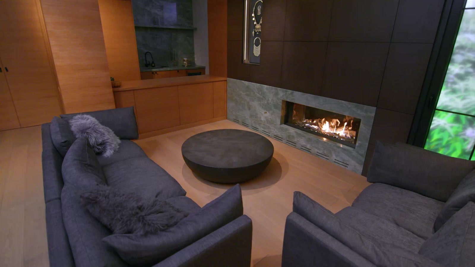 A long fireplace set into green-grey stone in a dark wood-panelled living room, two sofas around a round table