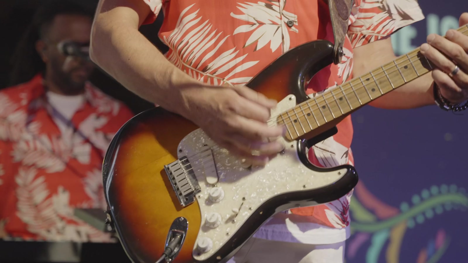 A guitarist in a floral shirt playing an electric guitar on stage