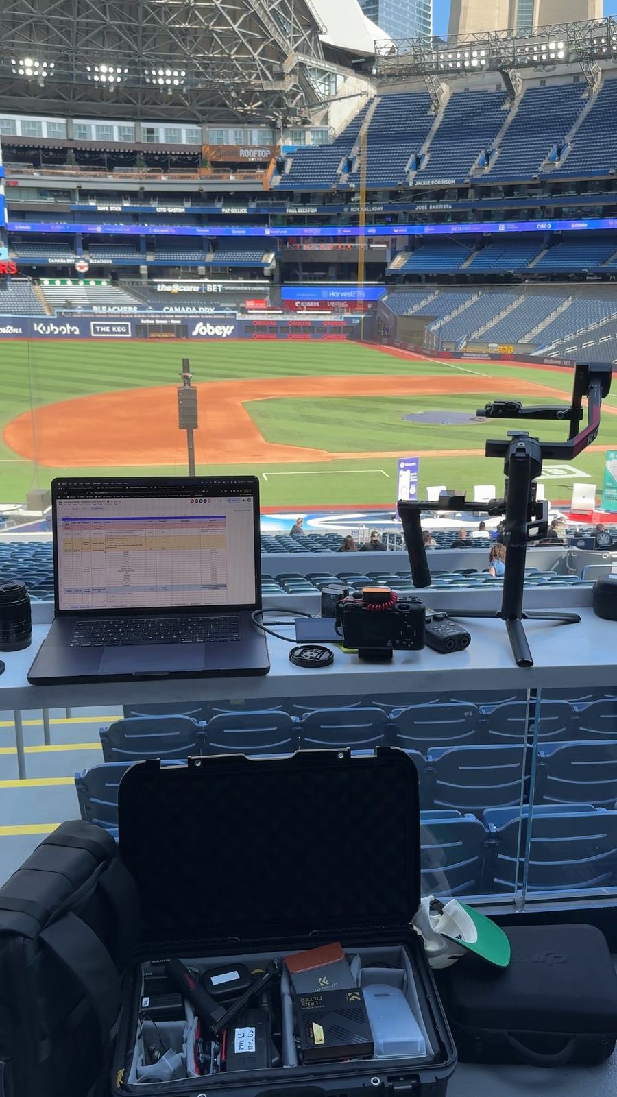 Laptop, camera equipment and an open kit case at a desk overlooking a stadium