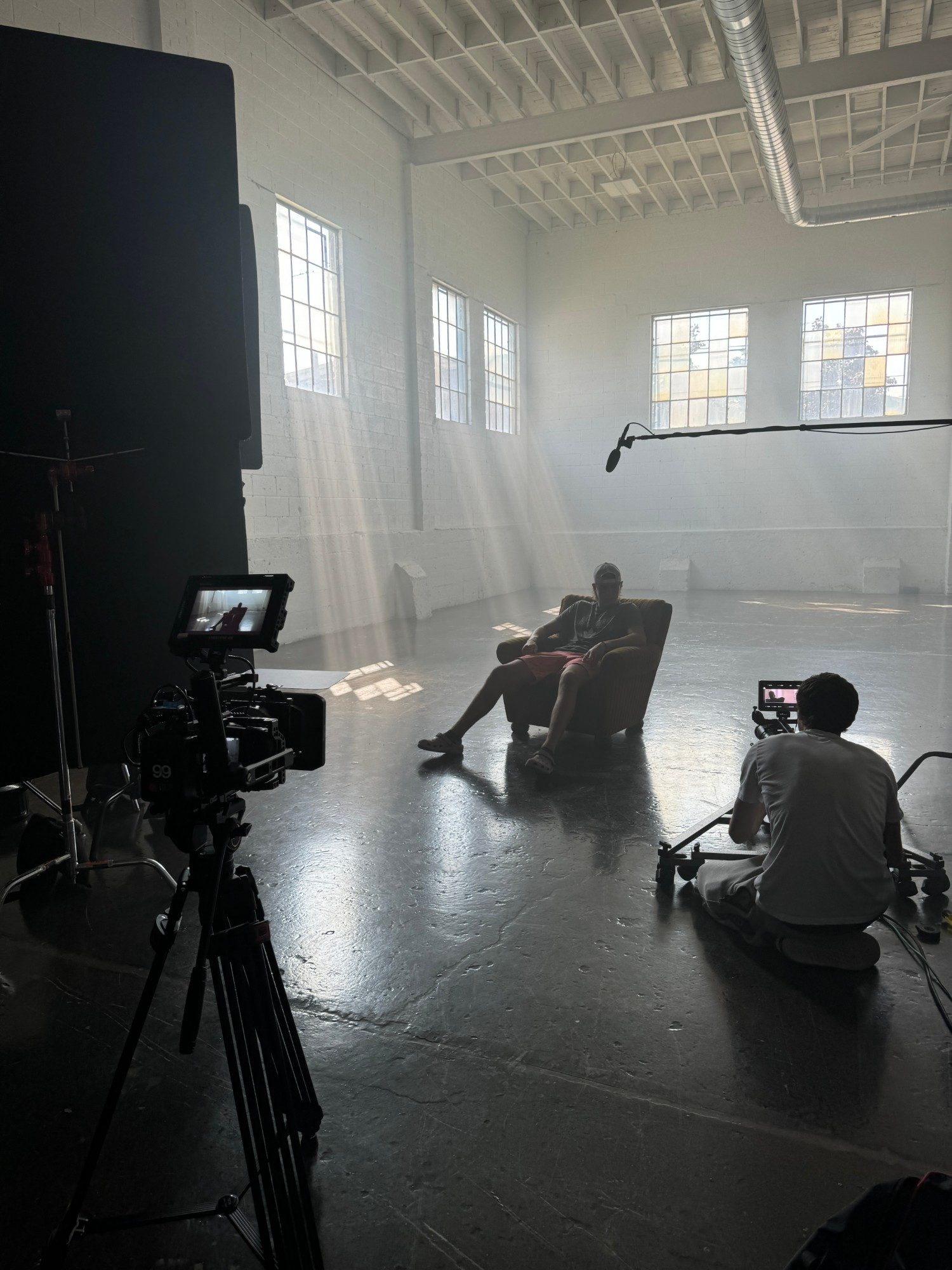 Two cameras filming a seated subject in a hazy white studio lit by window light