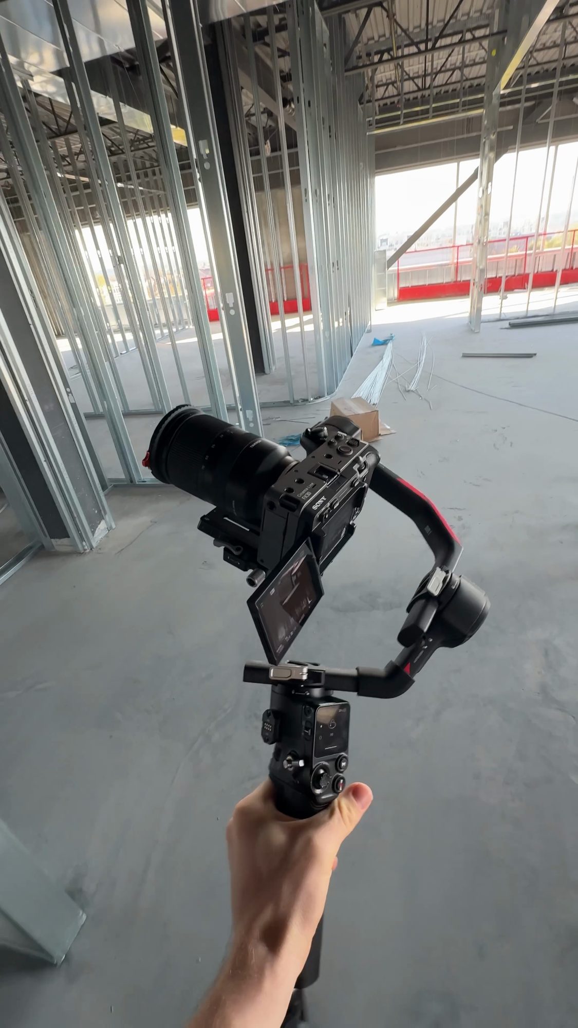 A camera on a gimbal held up in a building under construction, with steel wall studs and red safety railings behind