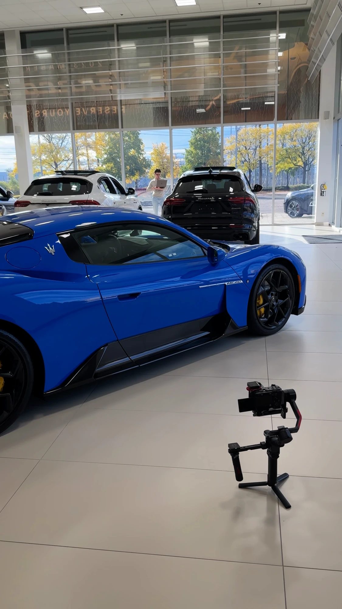 A camera on a gimbal beside a blue sports car in a car showroom