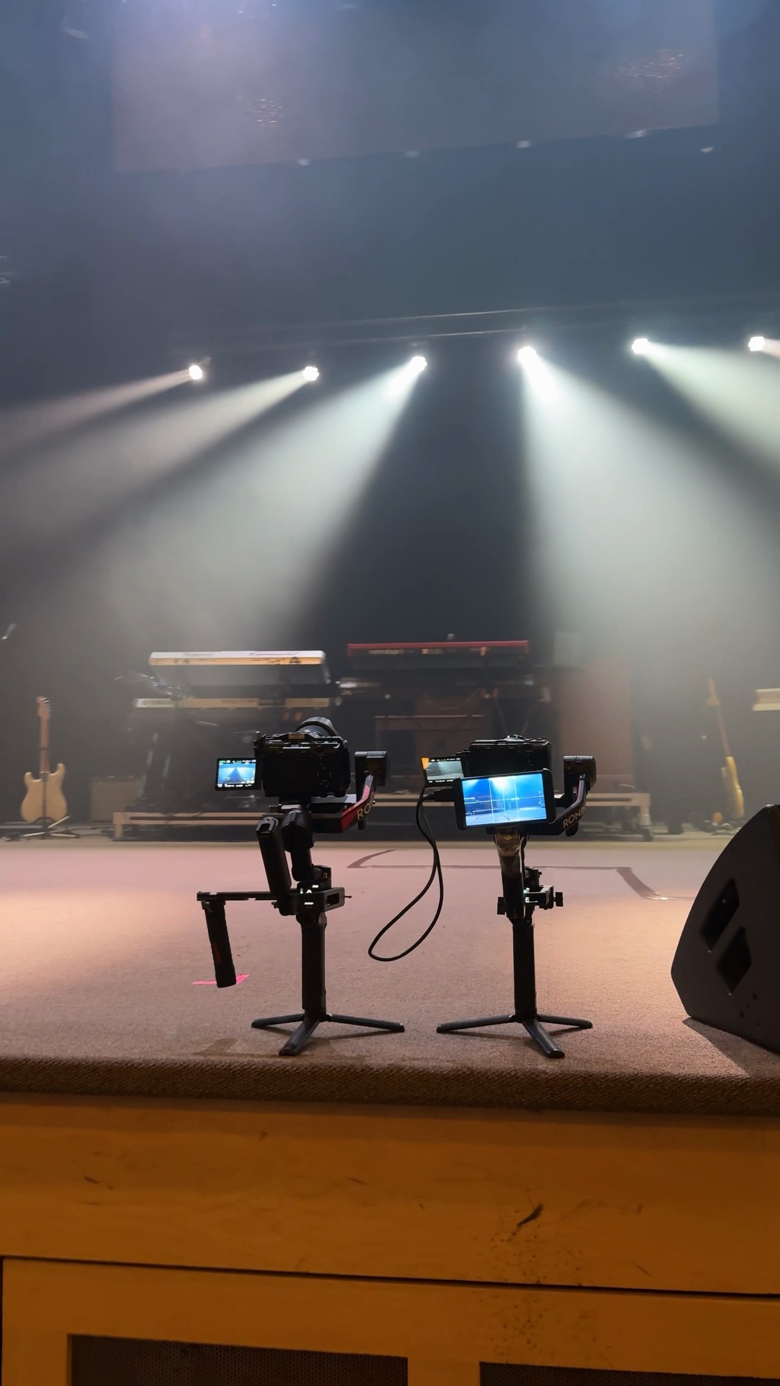 Two cameras on gimbals in front of a lit stage