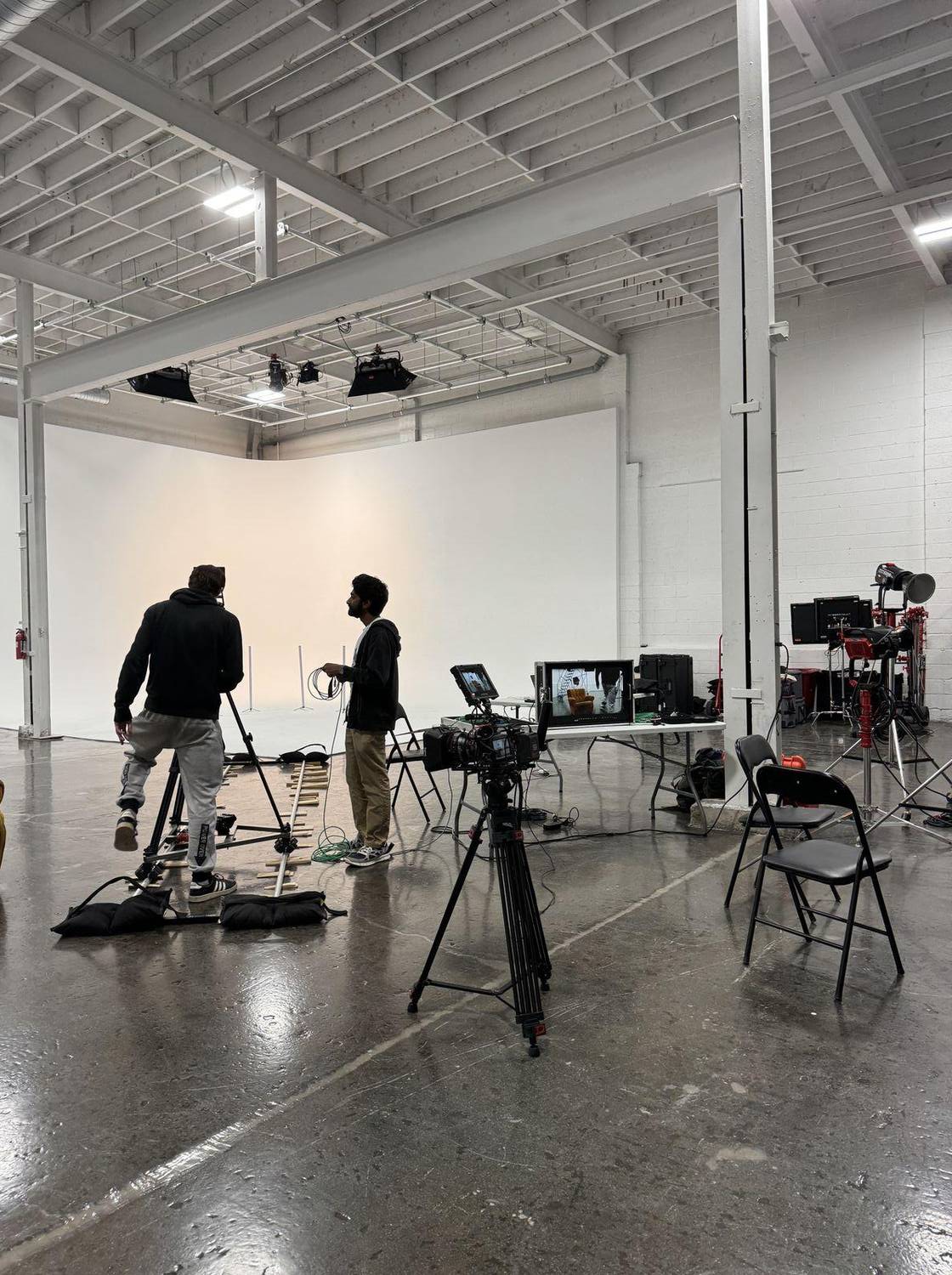Crew preparing cameras, a dolly track and lights on a white studio set