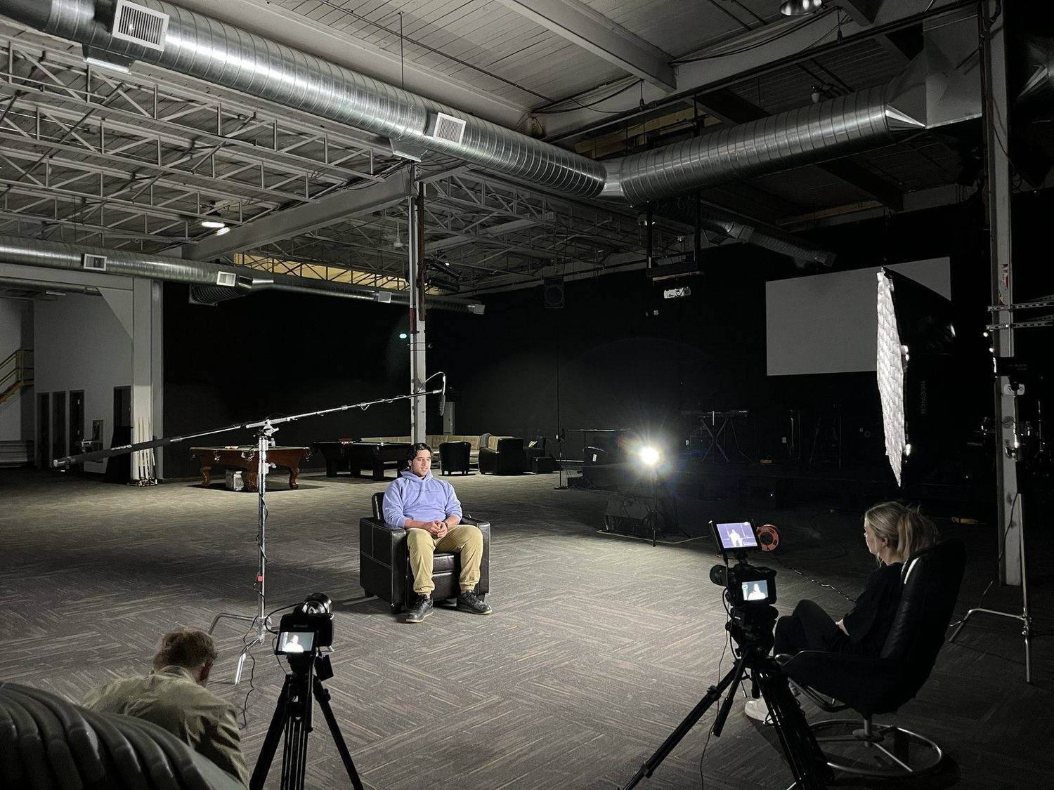 A wide studio set with cinema cameras, overhead rigging and large lights