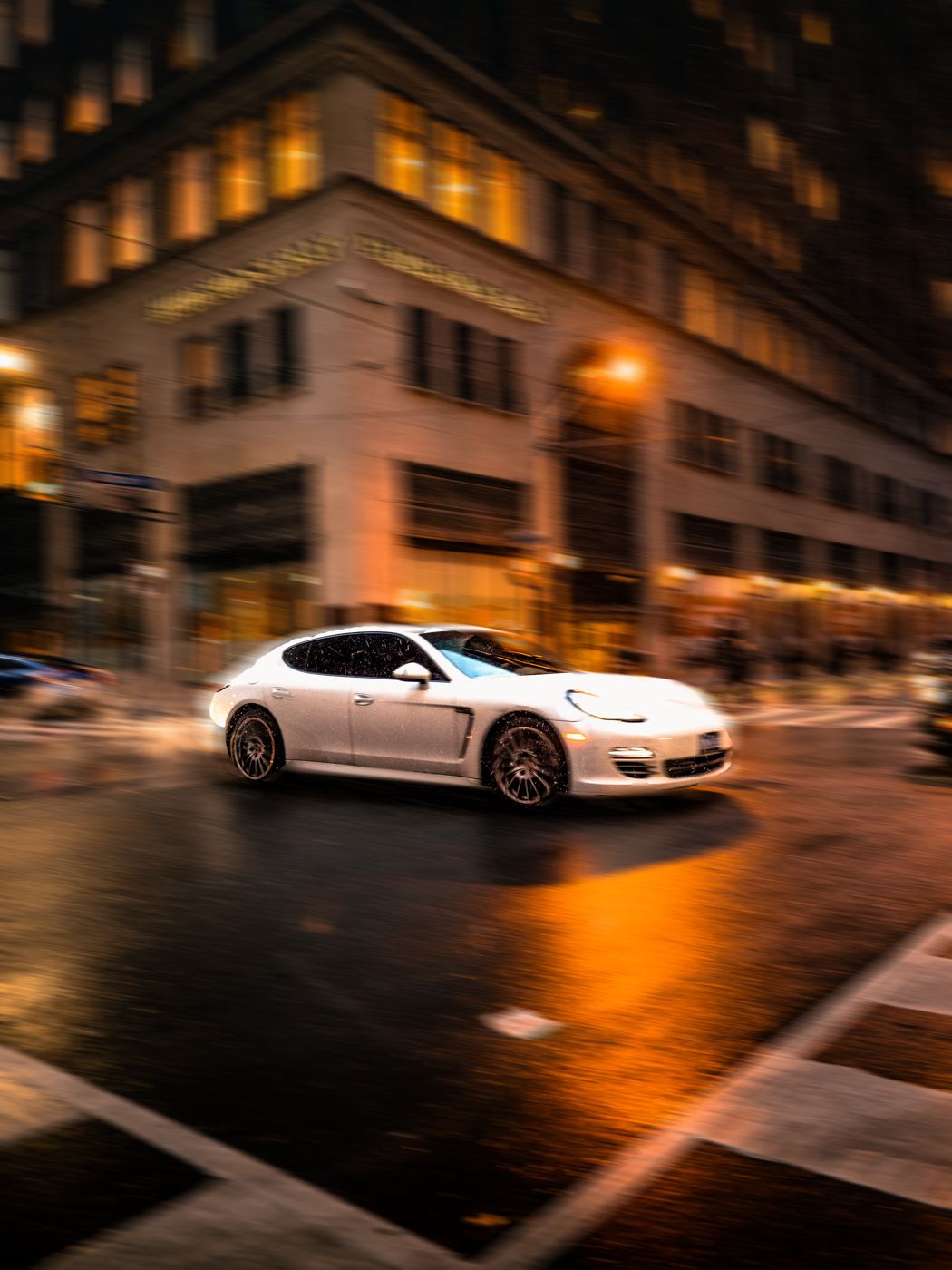 White sports car moving through a rain-soaked city street at night